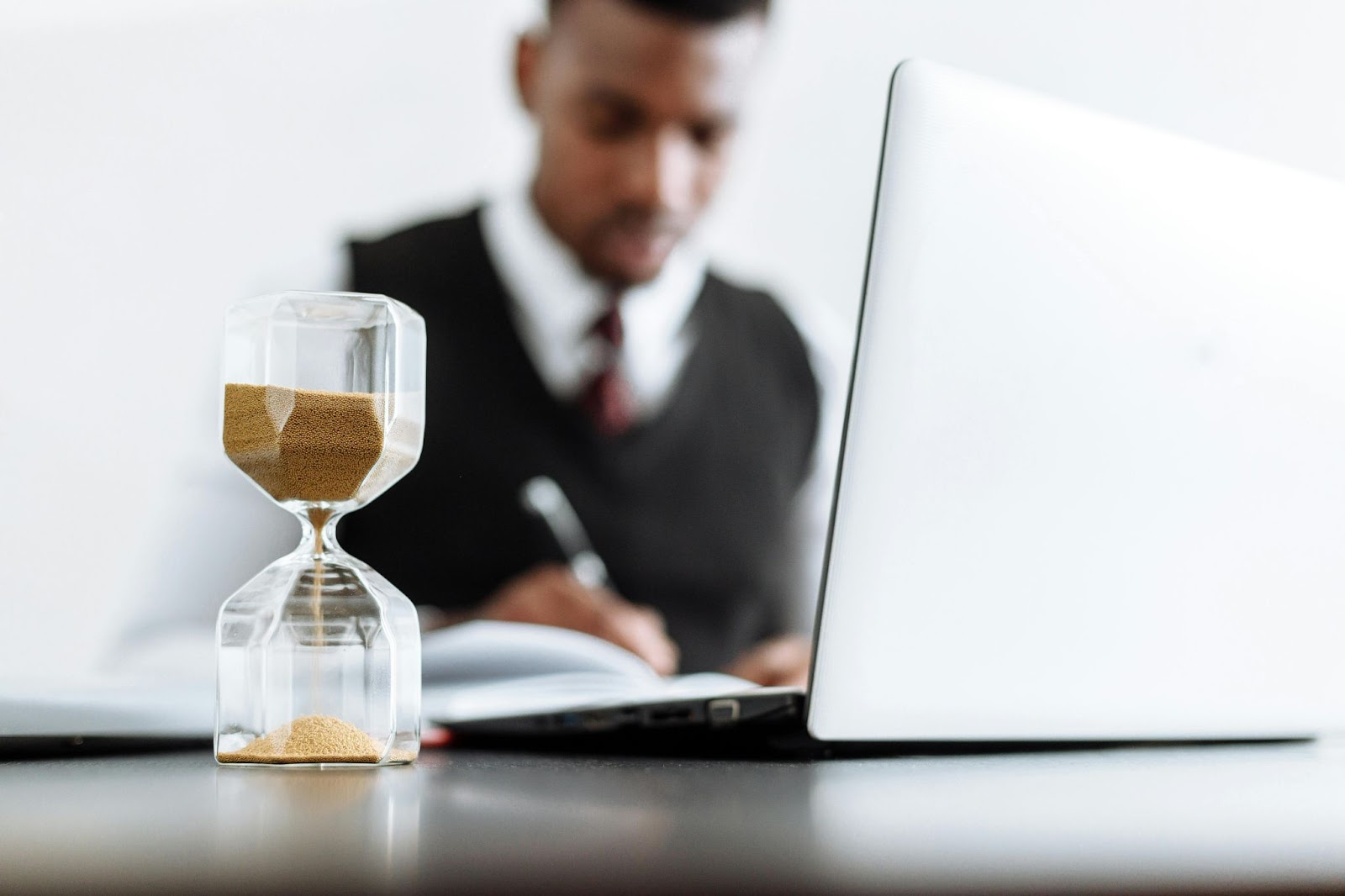 An hourglass in the foreground symbolizes time passing, while a businessman works in the background.